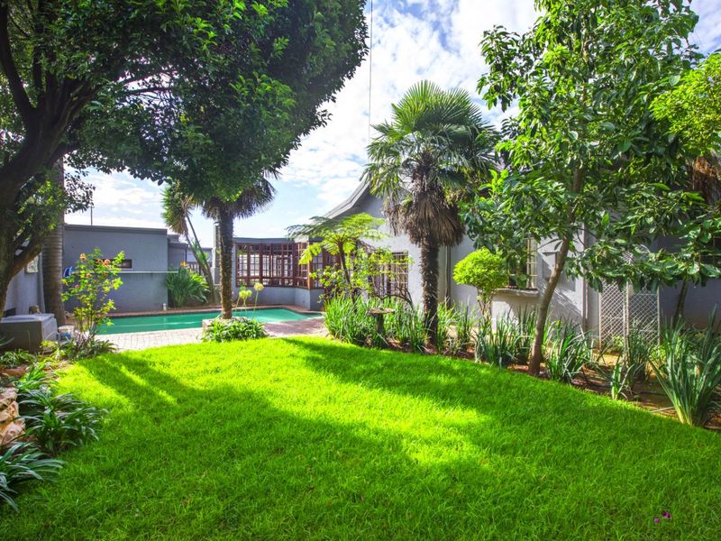 A well-maintained rear garden featuring a swimming pool, paved patio area, and established landscaping with mature trees.