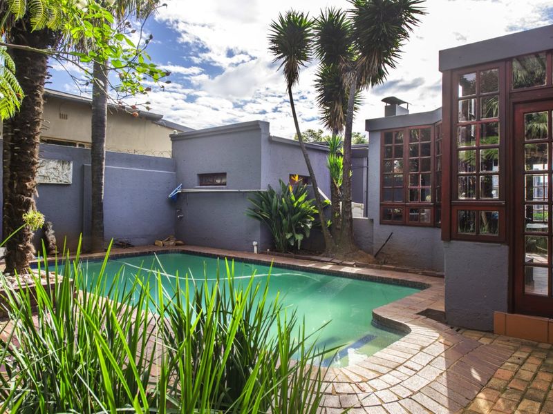 A private outdoor pool area featuring brick paving, established landscaping, and a modern grey-rendered building facade with timber-framed windows.