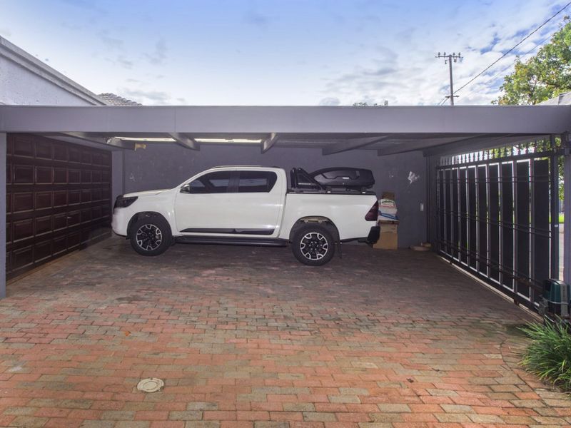 A covered carport area featuring paved flooring, a secure metal gate, and an adjacent enclosed garage section.