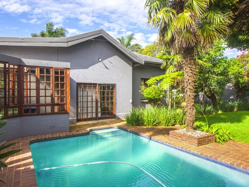 Rear exterior view featuring a swimming pool with brick coping, established garden, and access to the home via sliding glass doors and timber windows.