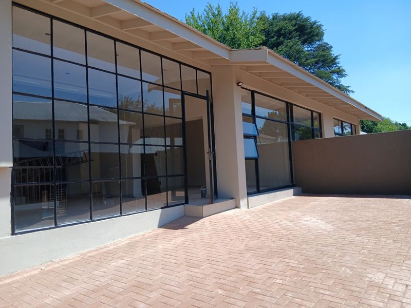 Rear exterior view featuring a paved patio area and large steel-framed glass windows providing seamless indoor-outdoor flow.