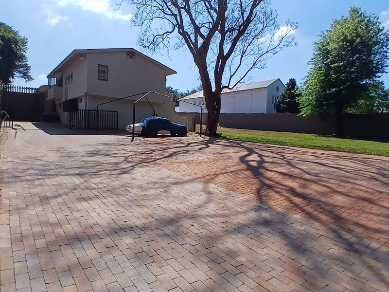 A spacious paved driveway leading to the side of the house, featuring a carport structure and perimeter boundary walls.