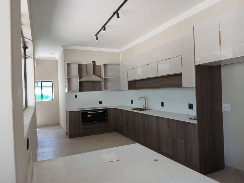 Modern kitchen featuring sleek two-tone cabinetry, stone countertops, integrated oven, extractor fan, and contemporary brass fixtures in a clean, open-plan layout.