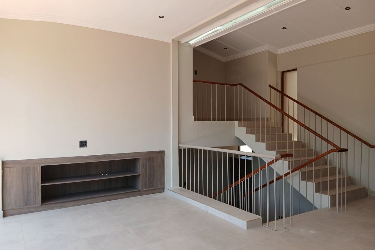 Spacious living area featuring neutral tiled flooring, built-in cabinetry, and an open staircase with a modern metal balustrade.