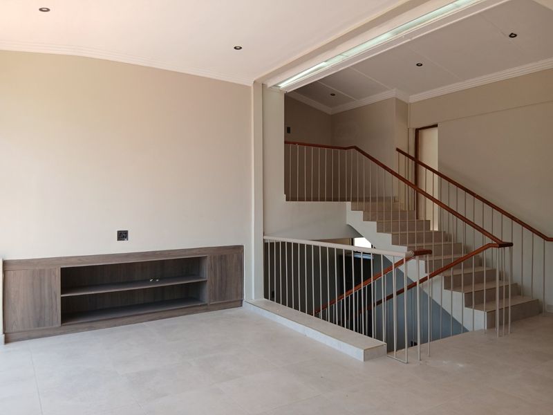 Spacious living area featuring neutral tiled flooring, built-in cabinetry, and an open staircase with a modern metal balustrade.