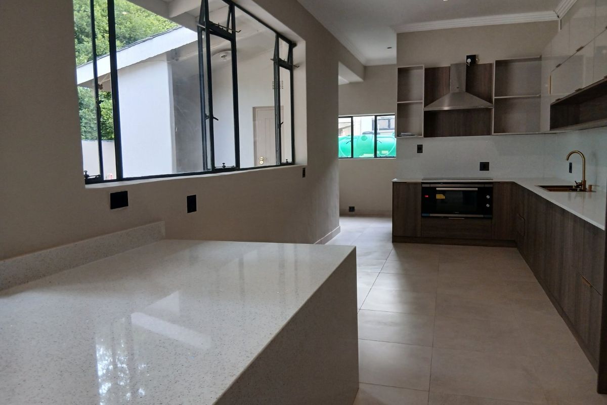Modern kitchen featuring sleek cabinetry, quartz countertops, built-in oven, extractor fan, and large windows providing ample natural light.