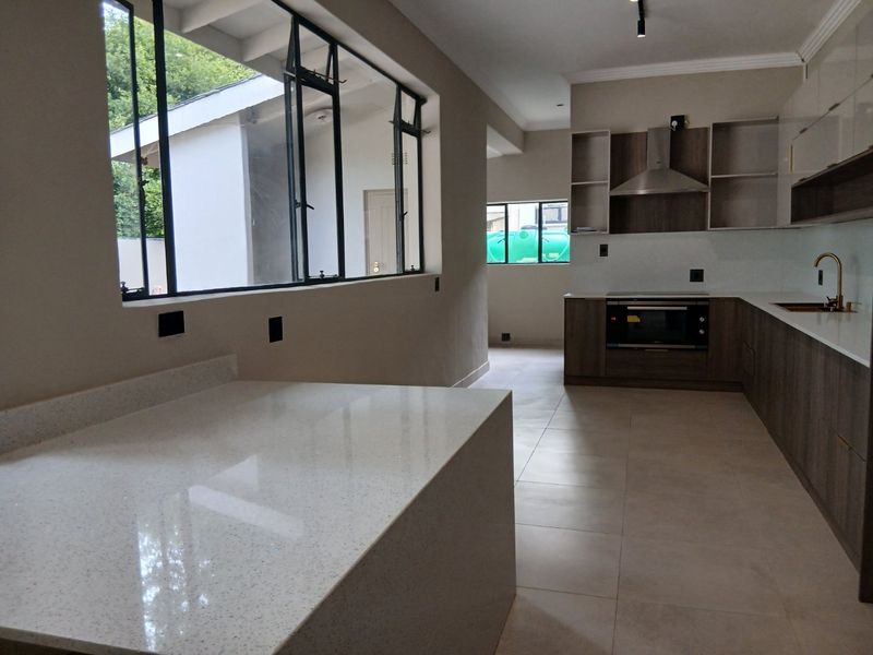 Modern kitchen featuring sleek cabinetry, quartz countertops, built-in oven, extractor fan, and large windows providing ample natural light.