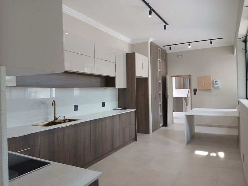 Modern kitchen featuring sleek two-tone cabinetry, stone countertops, brass fixtures, and a built-in breakfast bar, illuminated by contemporary track lighting.
