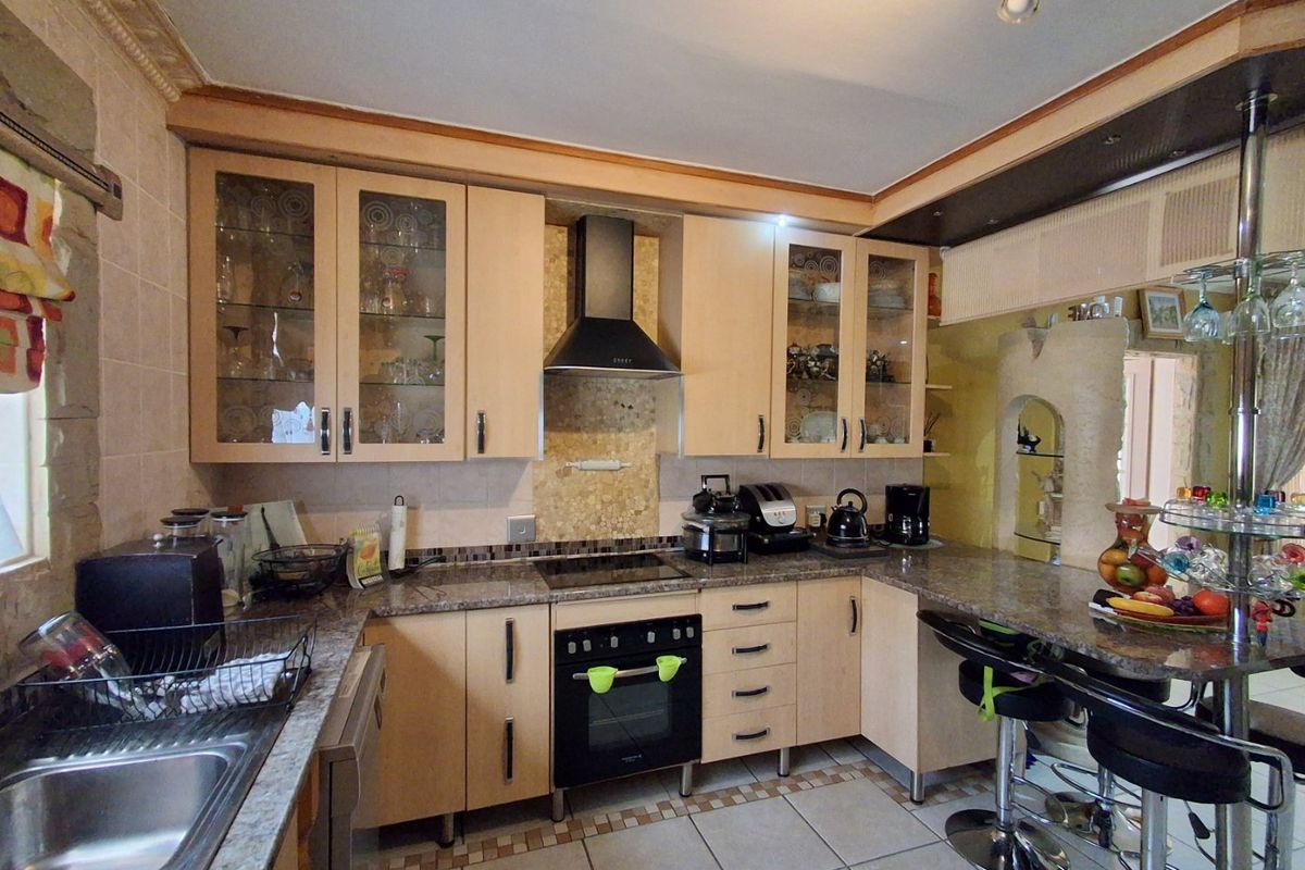 Functional kitchen featuring light wood cabinetry, granite countertops, integrated oven and hob, and a breakfast bar area with tiled flooring.