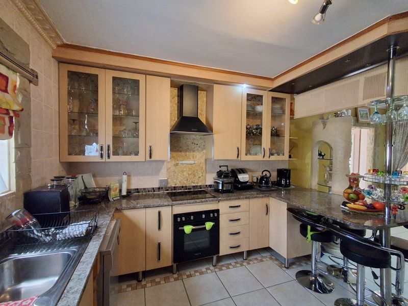 Functional kitchen featuring light wood cabinetry, granite countertops, integrated oven and hob, and a breakfast bar area with tiled flooring.