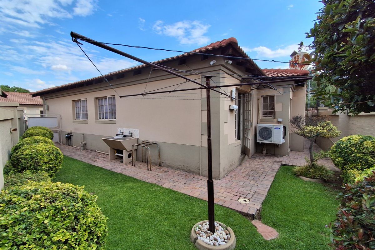 Rear exterior view of the townhouse featuring a paved walkway, small lawn, external wash basin, and an installed air conditioning unit.