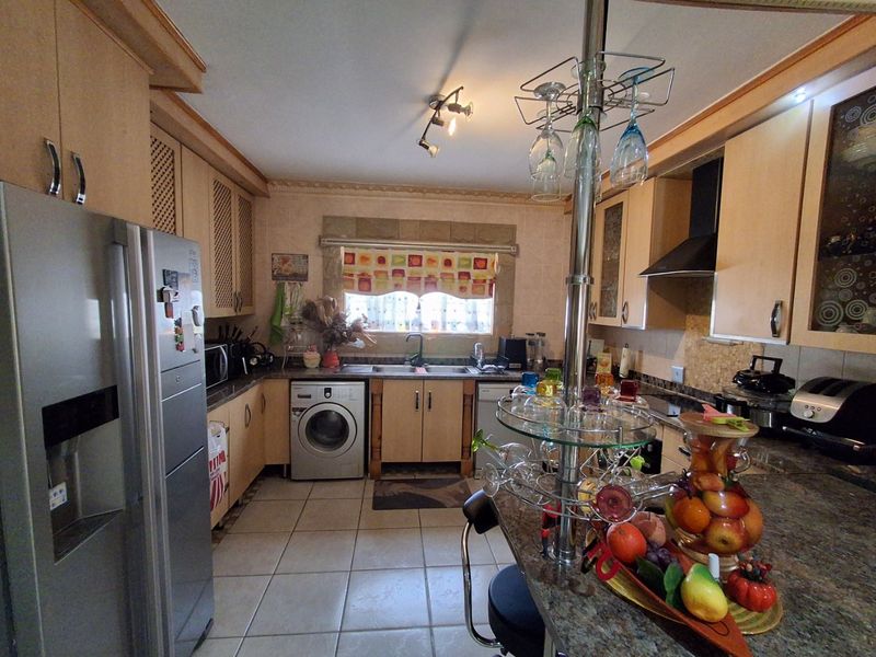 A functional kitchen featuring light wood cabinetry, granite countertops, a double basin sink, and integrated appliances with tiled flooring throughout.