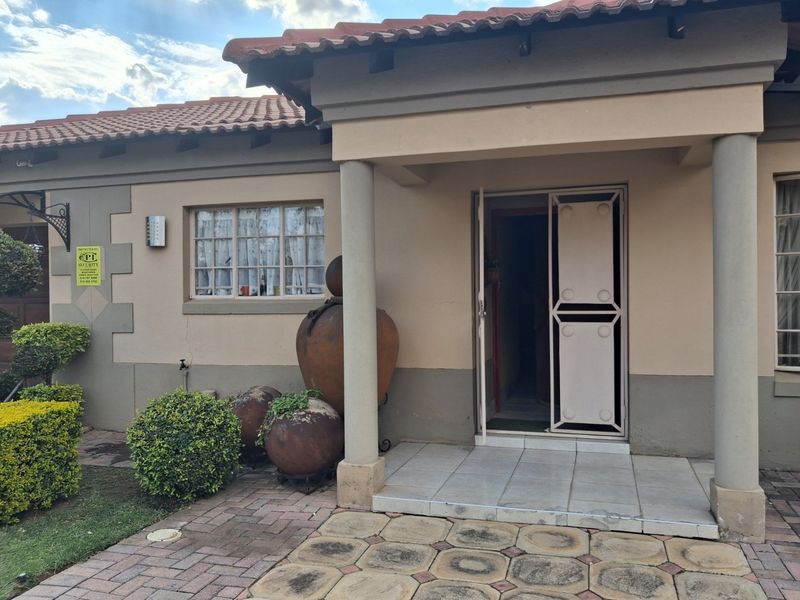 Front entrance of the townhouse featuring a covered porch, concrete columns, security gate, and paved driveway area.