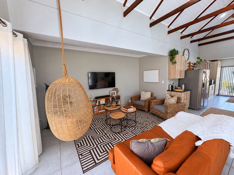 Spacious open-plan living area featuring high vaulted ceilings with exposed timber trusses, tiled flooring, and a modern integrated kitchen space.