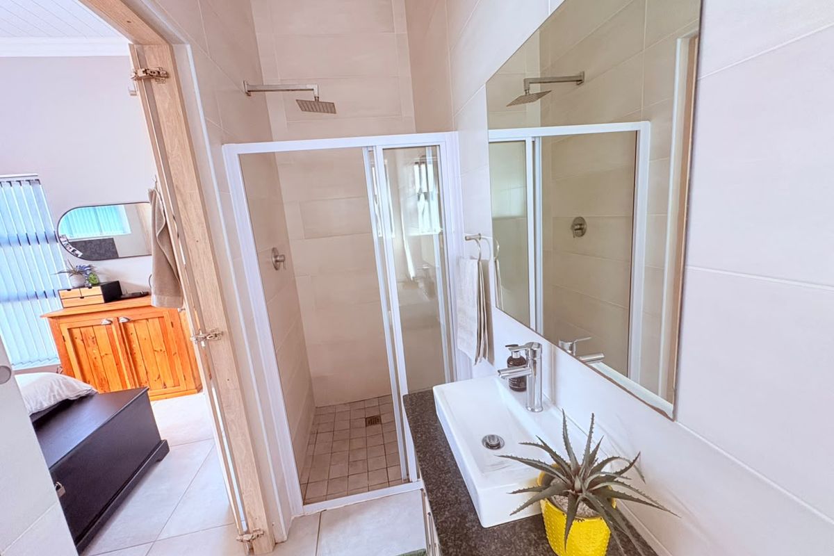 A modern bathroom featuring a glass-enclosed shower with a rain shower head, a sleek wall-mounted basin, and a large vanity mirror.