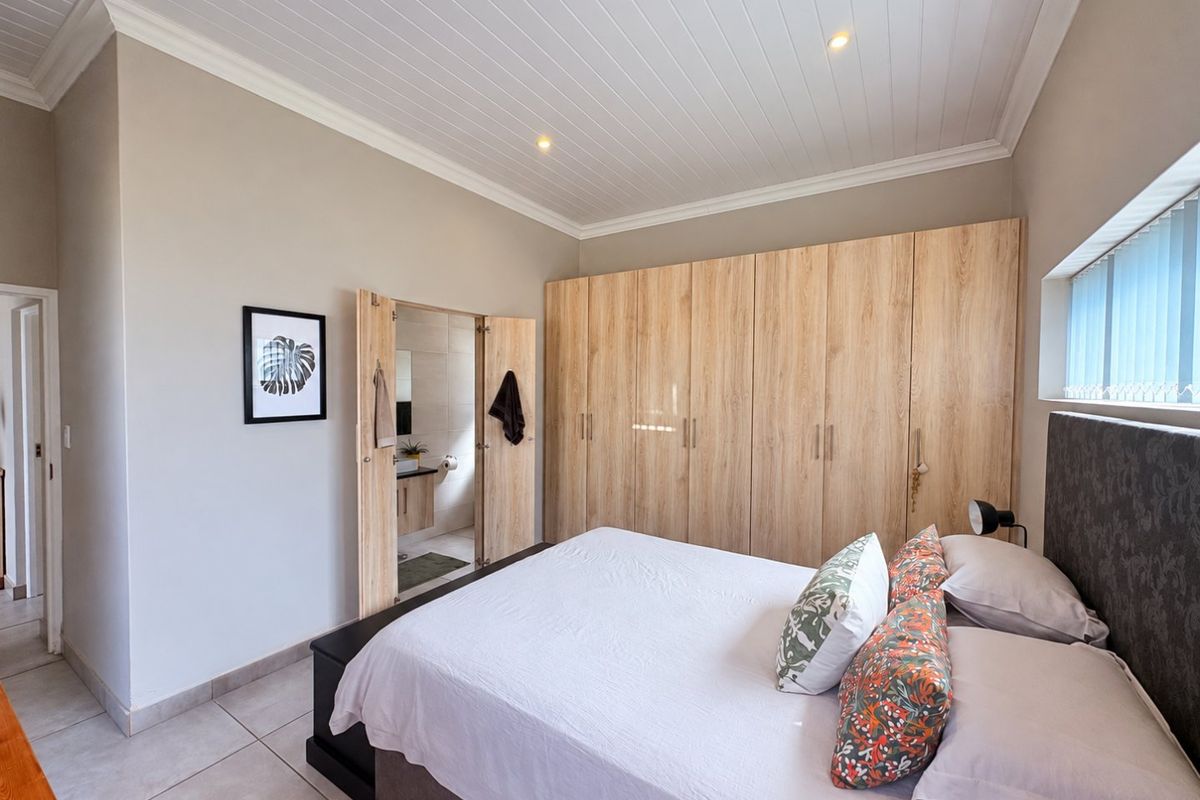 A well-maintained bedroom featuring extensive built-in wooden cupboards, tiled flooring, and a clean tongue and groove ceiling with recessed lighting.