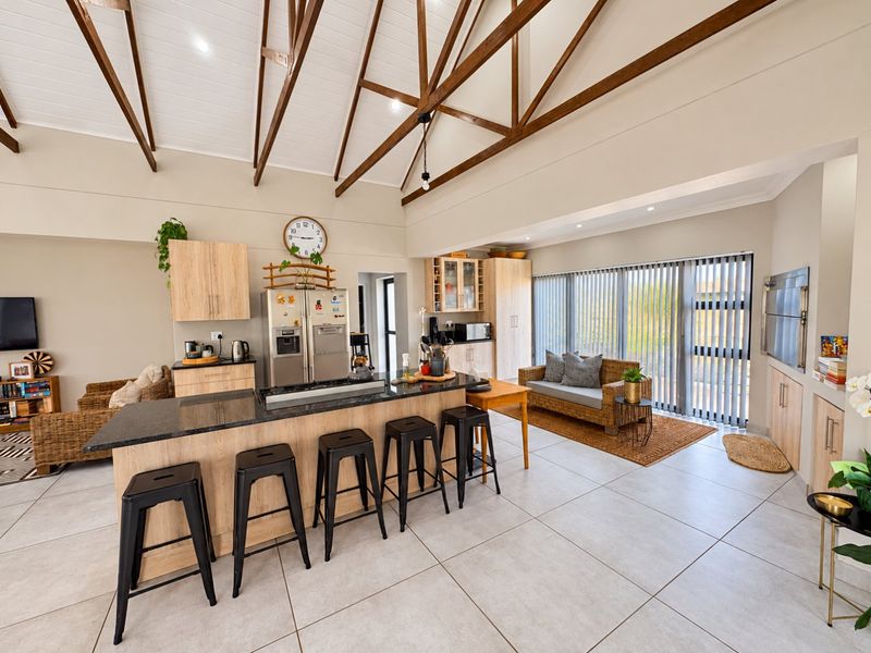 Spacious open-plan living and kitchen area featuring a high vaulted timber beam ceiling, modern granite island, and large windows with vertical blinds.