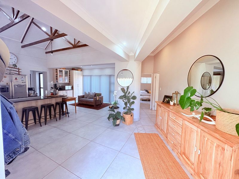 Spacious open-plan living area featuring high vaulted ceilings with exposed timber trusses, tiled flooring, and a modern kitchen island with integrated cabinetry.