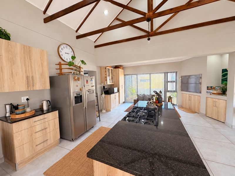 Spacious open-plan kitchen and living area featuring a vaulted ceiling with exposed timber trusses, granite island with gas hob, and a built-in indoor braai.