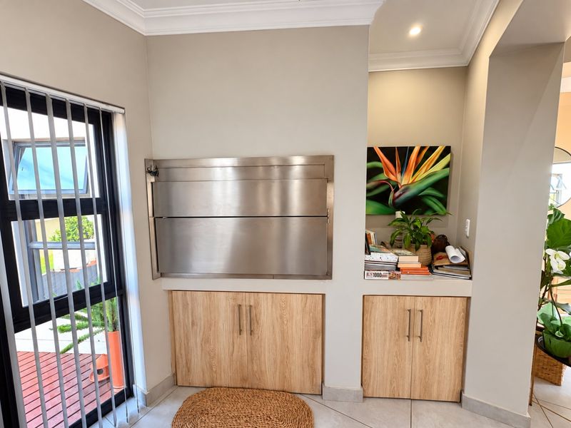 Indoor patio area featuring a built-in stainless steel braai, custom wood-finish cabinetry, and tiled flooring with access to an outdoor deck.