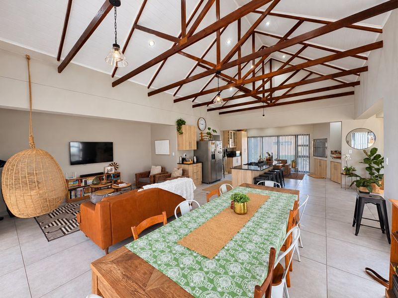 Spacious open-plan living, dining, and kitchen area featuring high vaulted ceilings with exposed timber trusses, modern tiled floors, and a functional kitchen island.