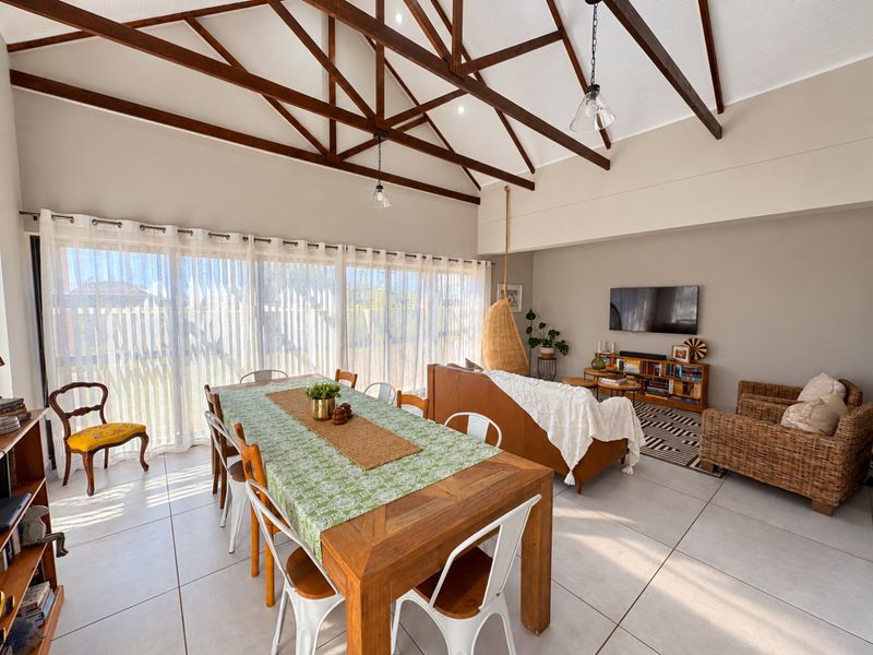 Spacious open-plan living and dining area featuring high vaulted ceilings with exposed timber trusses and large sliding glass doors providing ample natural light.