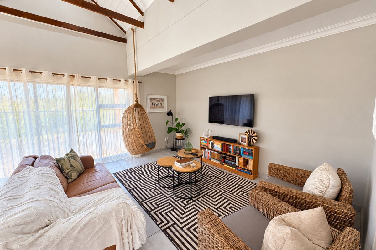 Spacious living room featuring a high vaulted ceiling with exposed timber beams, tiled flooring, and large sliding glass doors providing ample natural light.