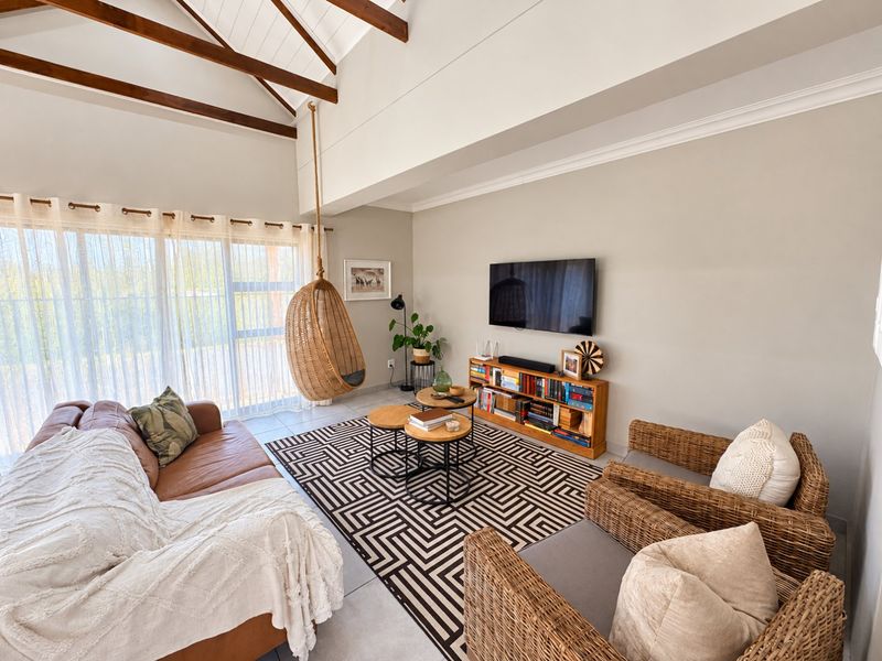 Spacious living room featuring a high vaulted ceiling with exposed timber beams, tiled flooring, and large sliding glass doors providing ample natural light.