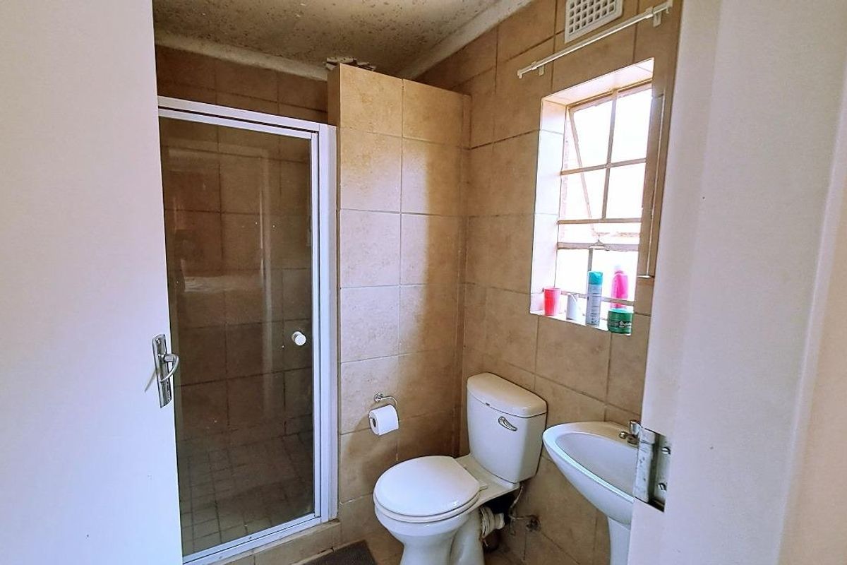 A compact bathroom featuring a shower enclosure, pedestal basin, and toilet with dated wall tiling and visible ceiling wear.