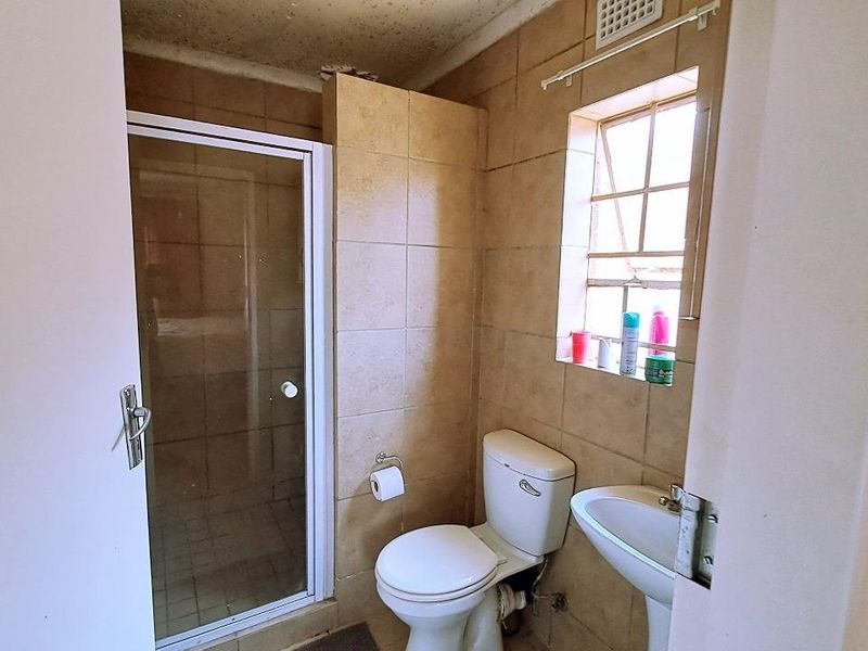 A compact bathroom featuring a shower enclosure, pedestal basin, and toilet with dated wall tiling and visible ceiling wear.