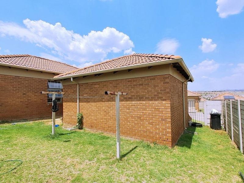 Rear view of the property featuring face brick exterior walls, a tiled roof, and a private garden area with a precast concrete boundary wall.