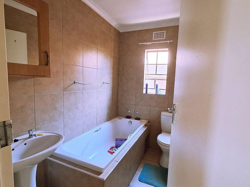 A functional bathroom featuring a pedestal basin, built-in bathtub, and toilet with neutral wall tiling.