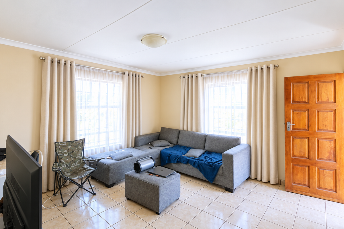 A living room featuring tiled flooring, coved ceilings, and a wooden panel door, providing a functional and neutral space for relaxation.