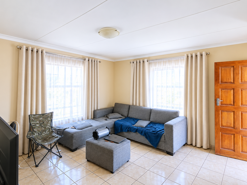 A living room featuring tiled flooring, coved ceilings, and a wooden panel door, providing a functional and neutral space for relaxation.