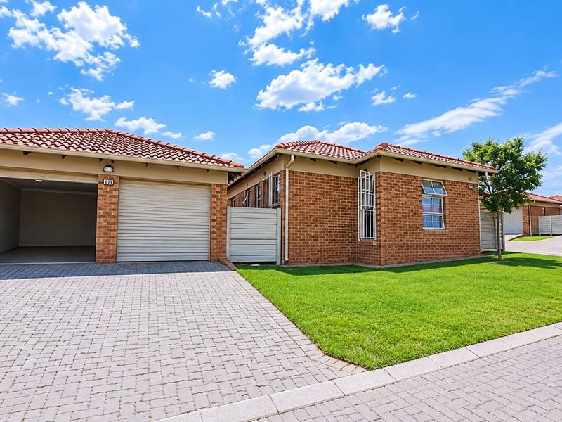 A well-maintained brick house featuring a double garage, paved driveway, and a neat front lawn under a clear blue sky.
