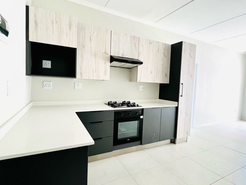 Modern open-plan kitchen featuring sleek two-tone cabinetry, stone countertops, integrated oven, gas hob, and extractor fan, set against neutral tiled flooring.