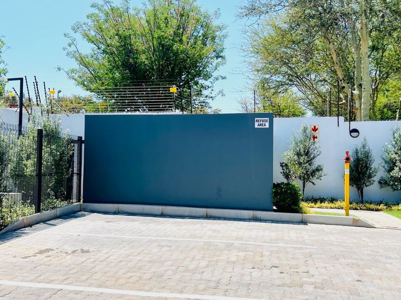 A clean and well-maintained utility area featuring paved parking, secure perimeter walling with electric fencing, and a designated refuse collection point.
