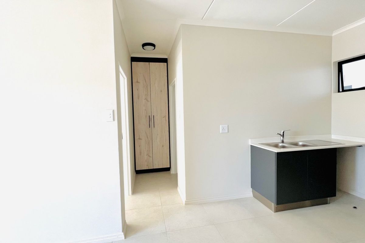A clean, modern kitchen area featuring built-in cabinetry, a sink, and a tall storage cupboard in a neutral, minimalist space.