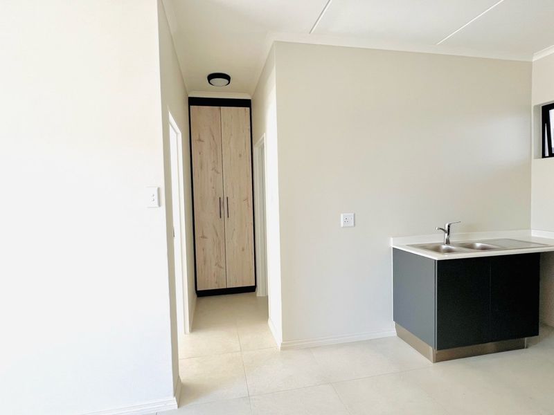 A clean, modern kitchen area featuring built-in cabinetry, a sink, and a tall storage cupboard in a neutral, minimalist space.
