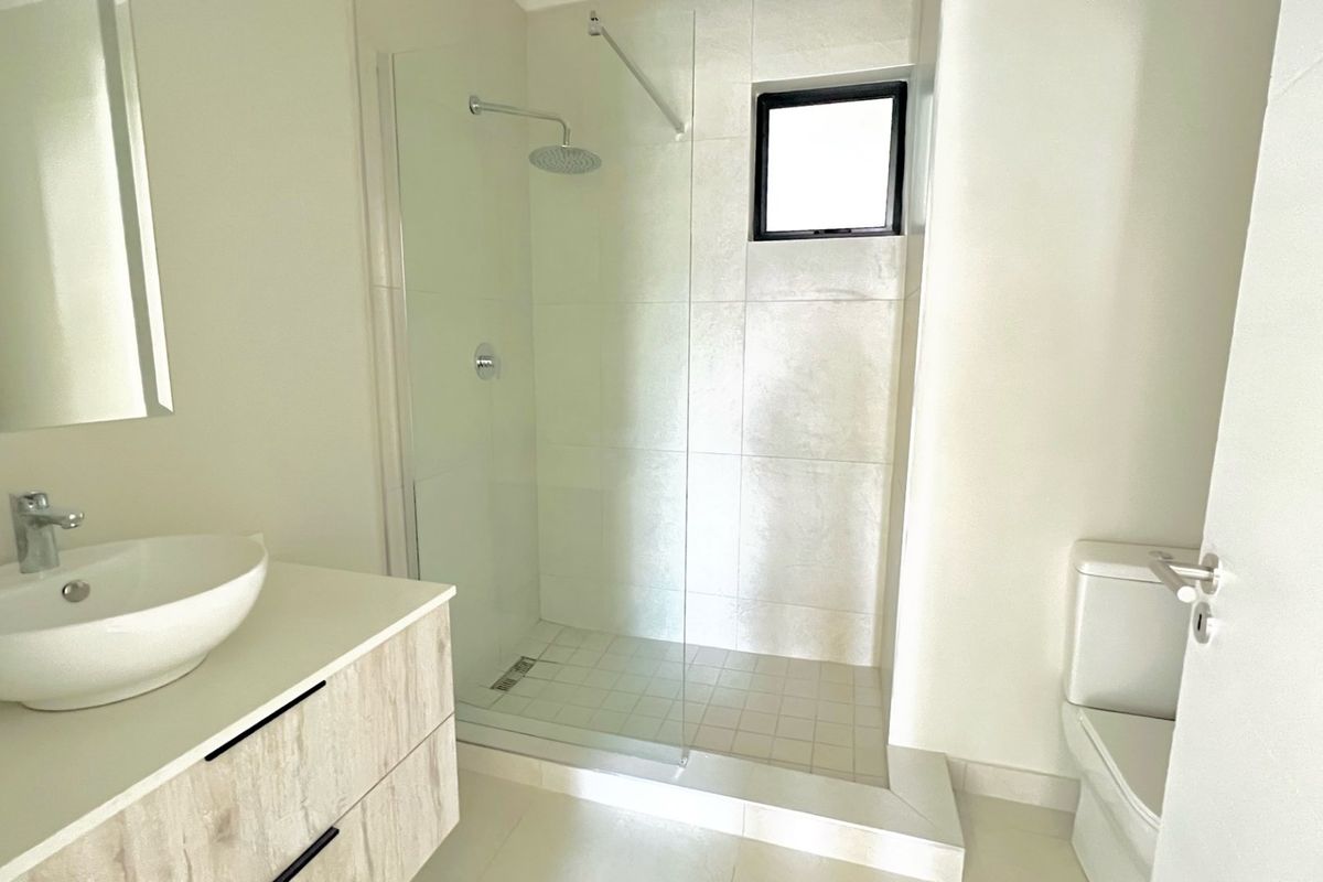 A modern, clean bathroom featuring a walk-in shower with glass screen, a contemporary vessel sink on a vanity cabinet, and a toilet.