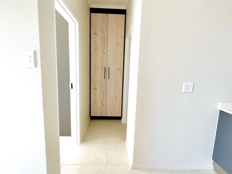 A clean, neutral hallway featuring light-toned tiled flooring and a modern built-in cupboard with wood-grain finish.