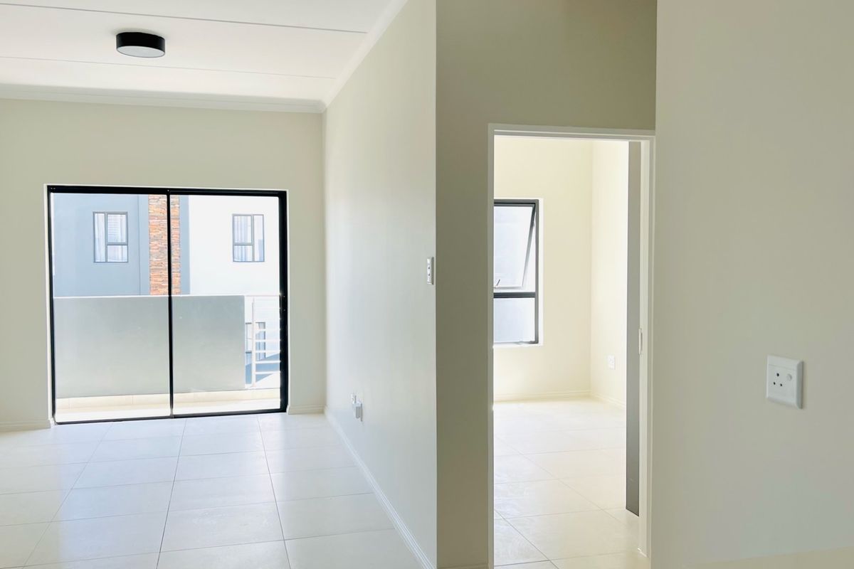 A bright, empty living area featuring neutral tiled flooring, a sliding glass door leading to a balcony, and a clean, modern interior finish.