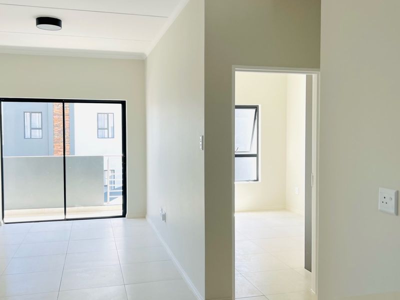A bright, empty living area featuring neutral tiled flooring, a sliding glass door leading to a balcony, and a clean, modern interior finish.