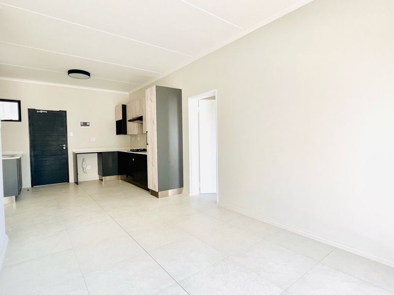 An open-plan living and kitchen area featuring modern cabinetry, a built-in hob, and neutral tiled flooring in a bright, vacant space.
