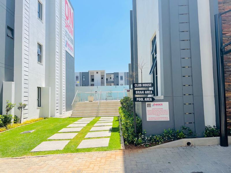 A well-maintained outdoor common area featuring a paved walkway, landscaped lawn, and concrete stairs leading to a communal facility area with glass balustrades.