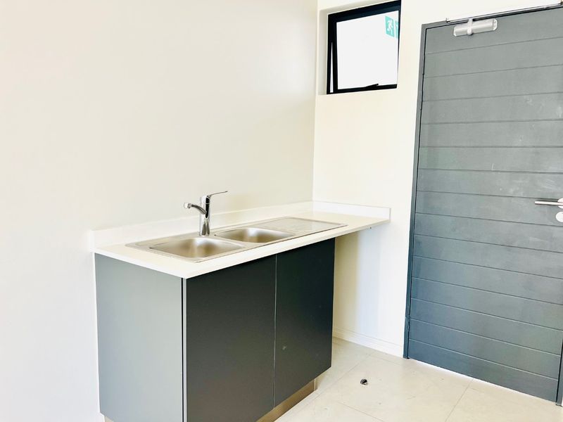 A clean, modern scullery or utility area featuring a stainless steel double sink, built-in base cabinetry, and tiled flooring.