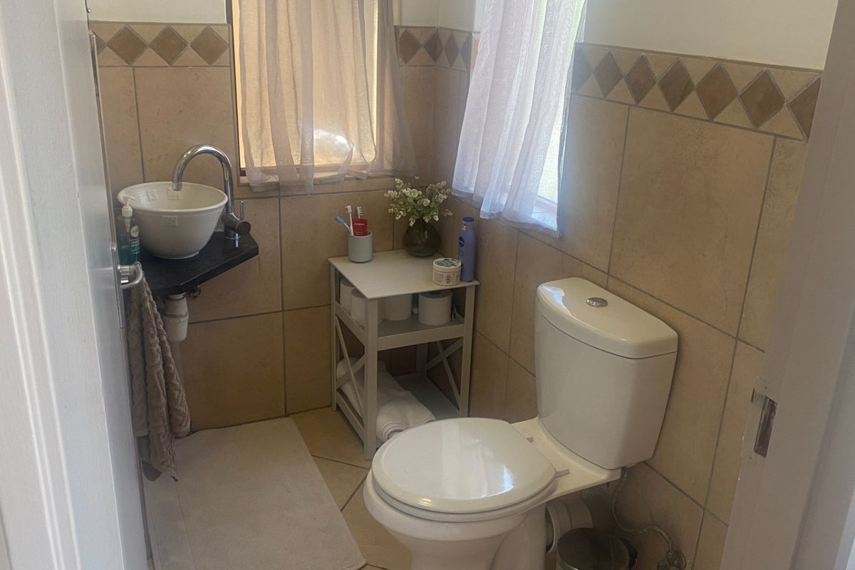 A compact bathroom featuring a white toilet, a modern vessel sink with a chrome faucet, and neutral-toned wall tiles with a decorative border.