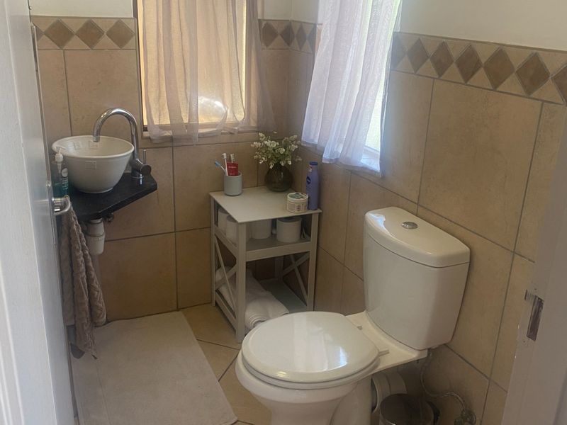 A compact bathroom featuring a white toilet, a modern vessel sink with a chrome faucet, and neutral-toned wall tiles with a decorative border.