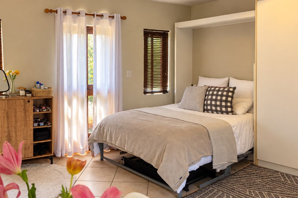 A well-lit bedroom featuring tiled flooring, built-in wardrobe storage, and timber venetian blinds with access to an outdoor area.