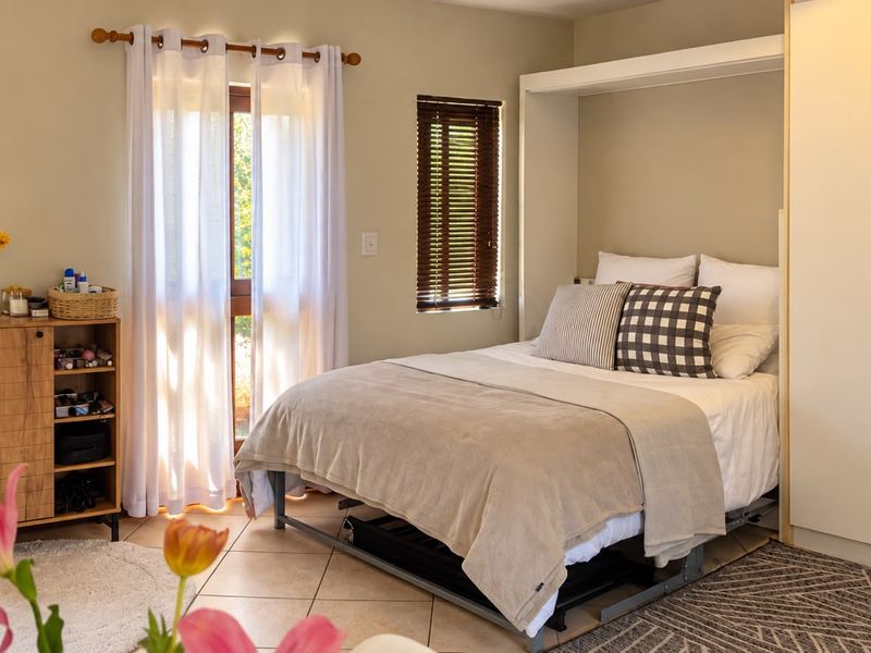 A well-lit bedroom featuring tiled flooring, built-in wardrobe storage, and timber venetian blinds with access to an outdoor area.